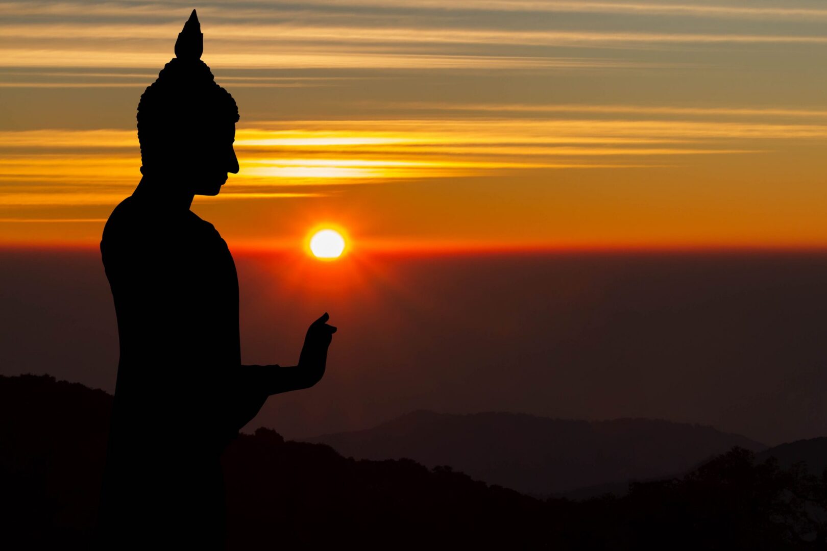 Silhouette of Buddha at sunset with mountains.